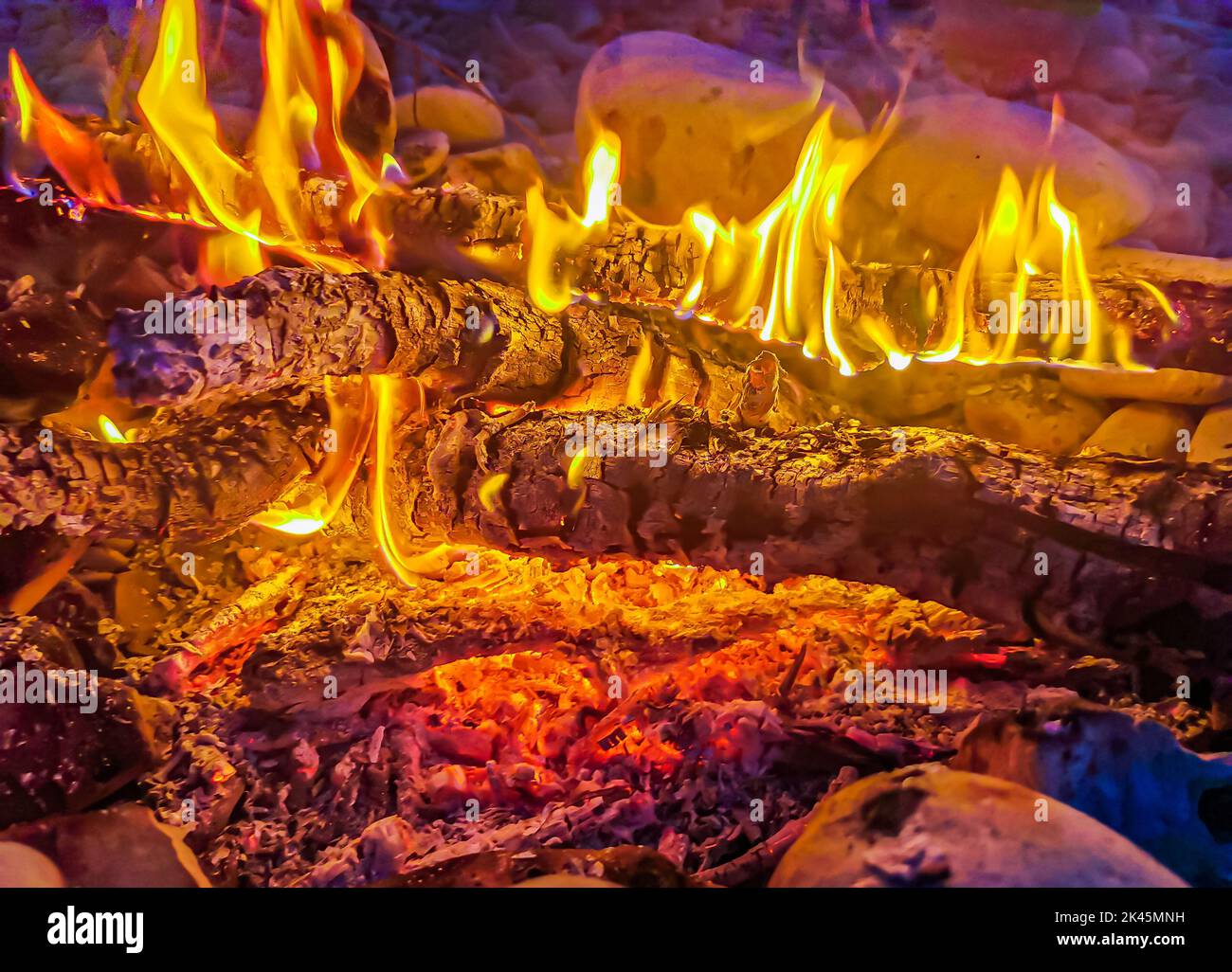A bonfire with glowing pieces of wood over a rocky river at night Stock