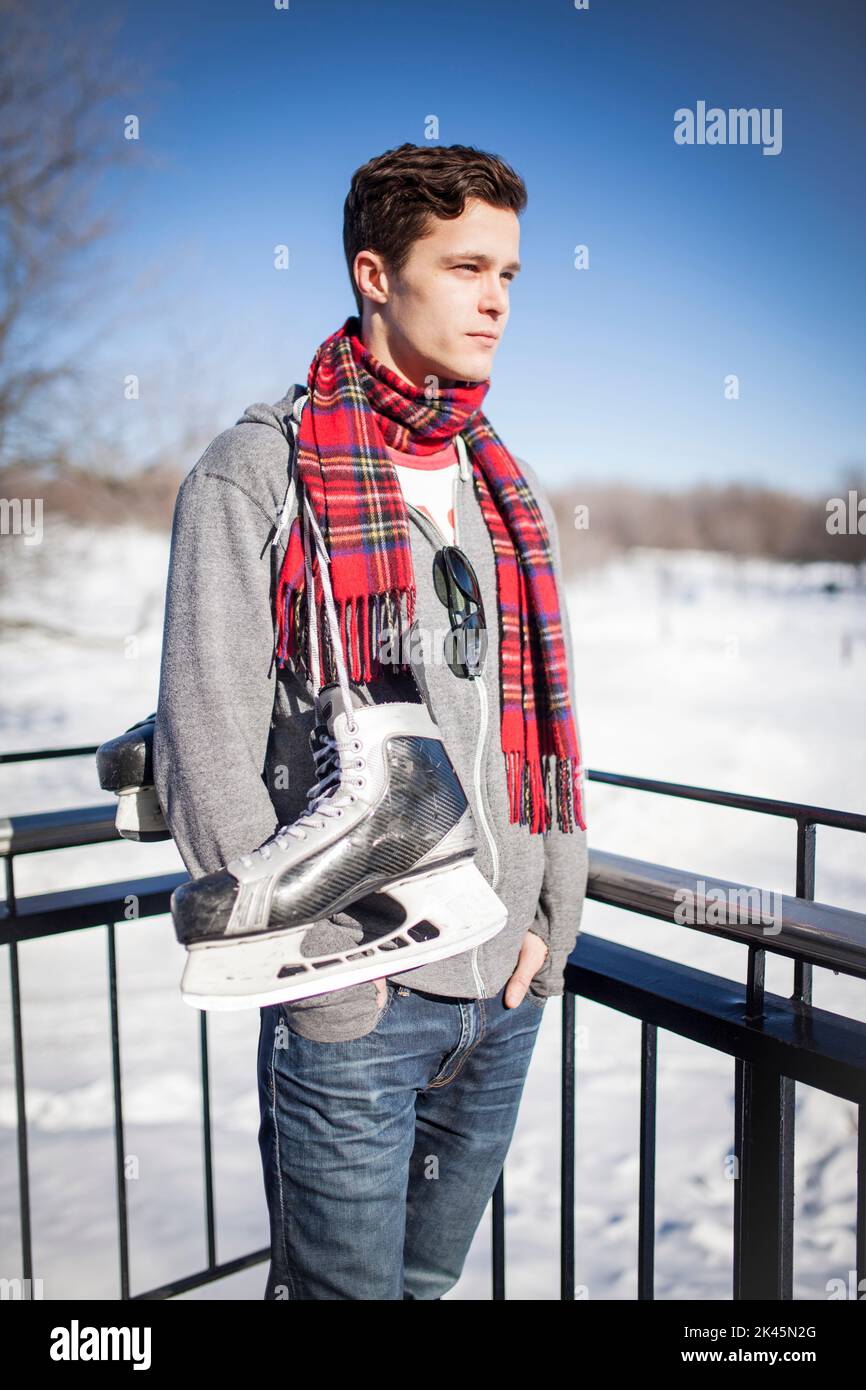 Man standing in snow with ice skates hanging around his neck. Stock Photo