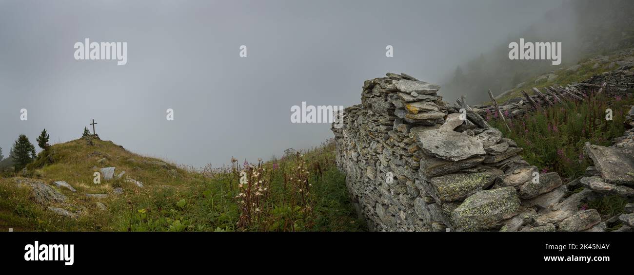 A mountain shrine by the path in the Alpine region near Mont Blanc, a cross near Fenetre D'Arpette, low clouds and mist. Stock Photo