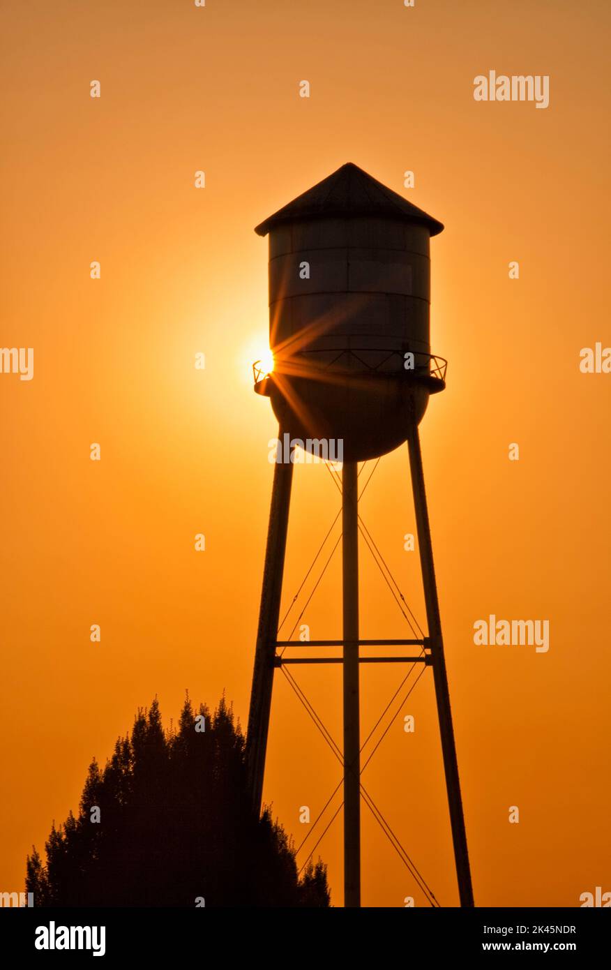 Sun setting behind agricultural water tower. Stock Photo