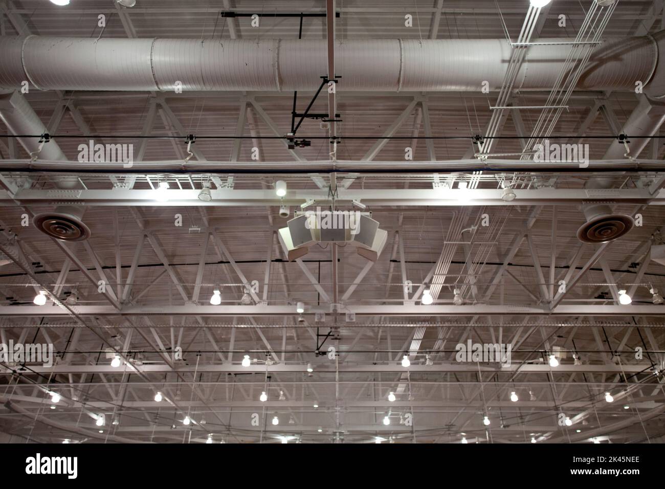 The ceiling of a large building, with air ducts and pipes, the rafters, gantry and struts, sound system speakers, lights and extractor units. Stock Photo