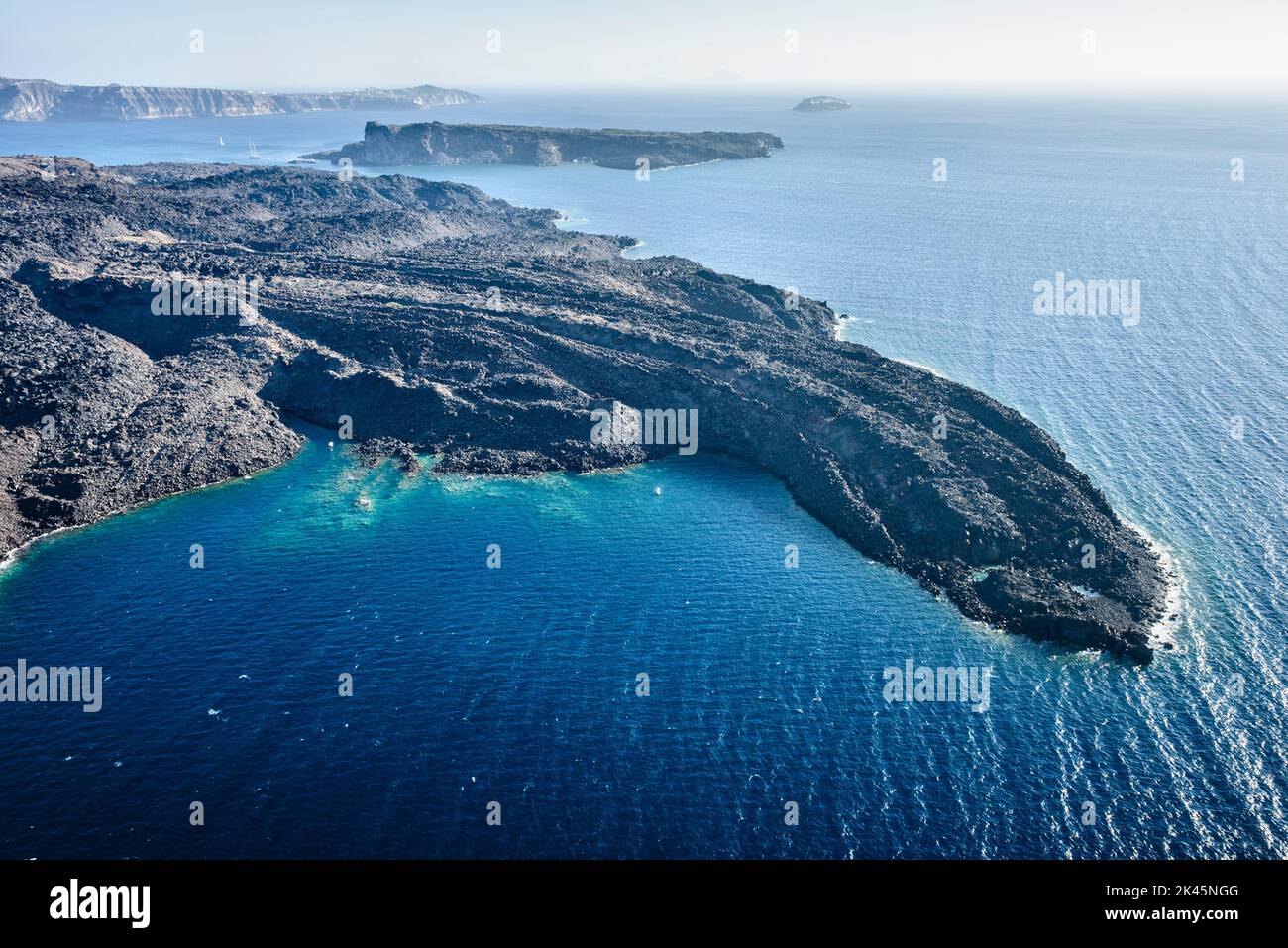 Aerial view of a headland on a island in the Aegean sea, volcanic rock formations, black ridges and small quiet inlets and islands. Boats in the dista Stock Photo