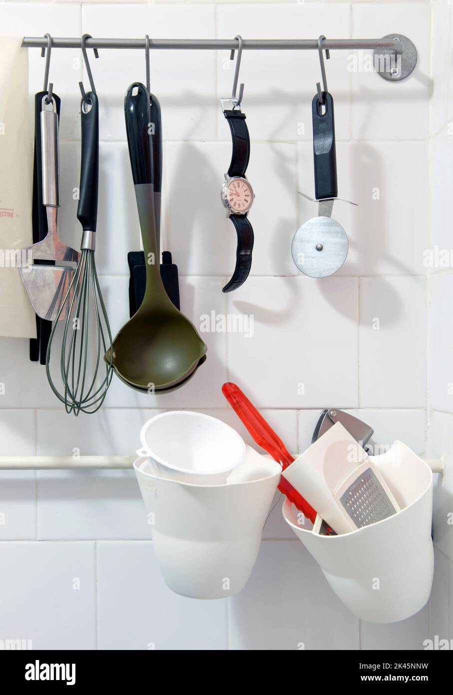 Wristwatch hanging on a rack amongst various kitchen tools Stock Photo