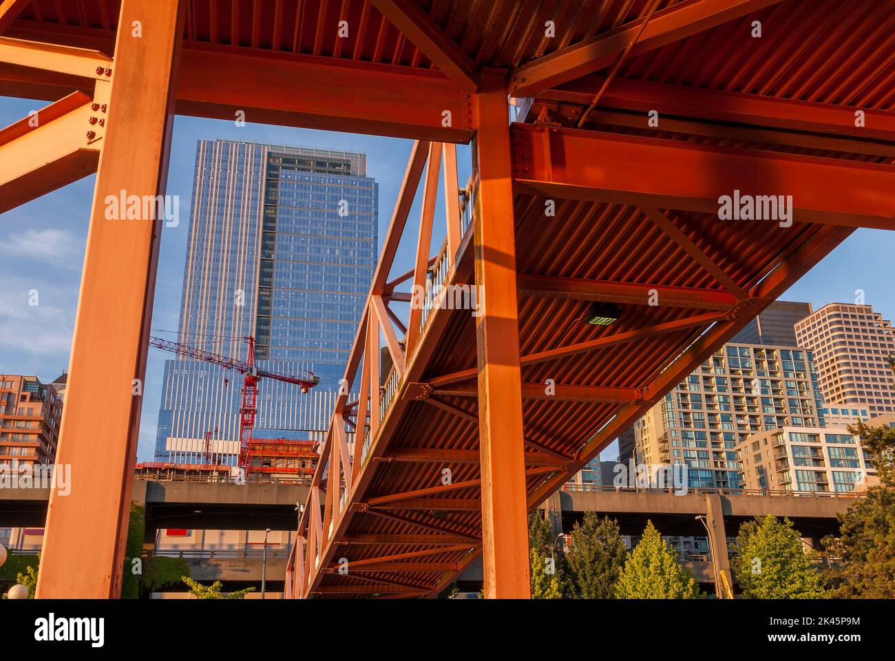 Red bridge seen from below with high rise buildings and contruction sites in background. Stock Photo