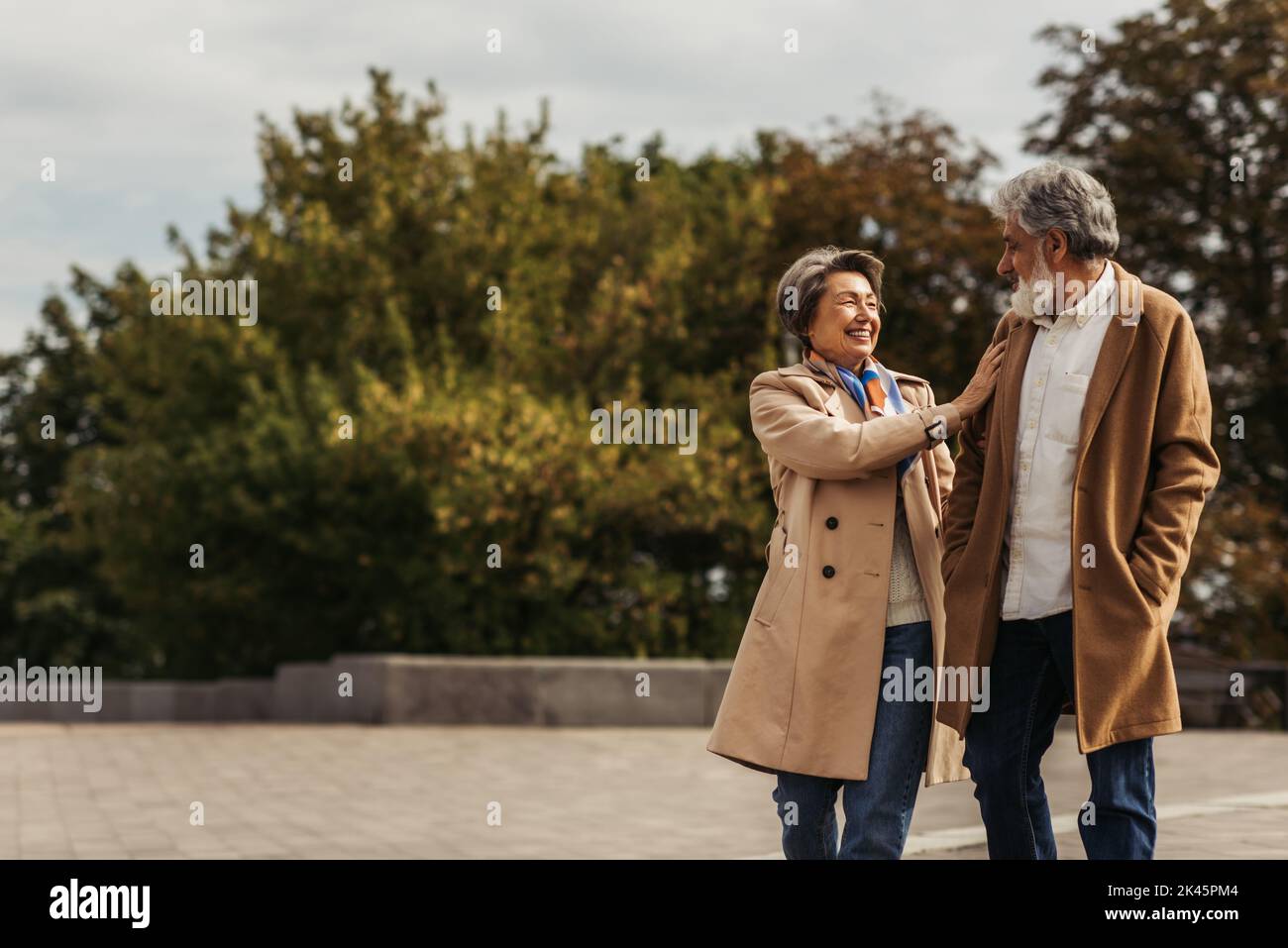 joyful senior woman hugging bearded husband in beige coat and standing ...