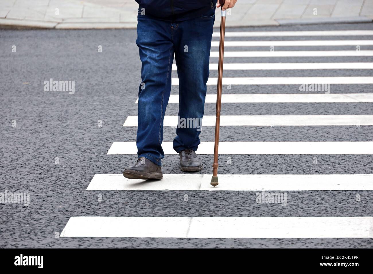 Man walking with a cane on crosswalk. Male legs on pedestrian crossing