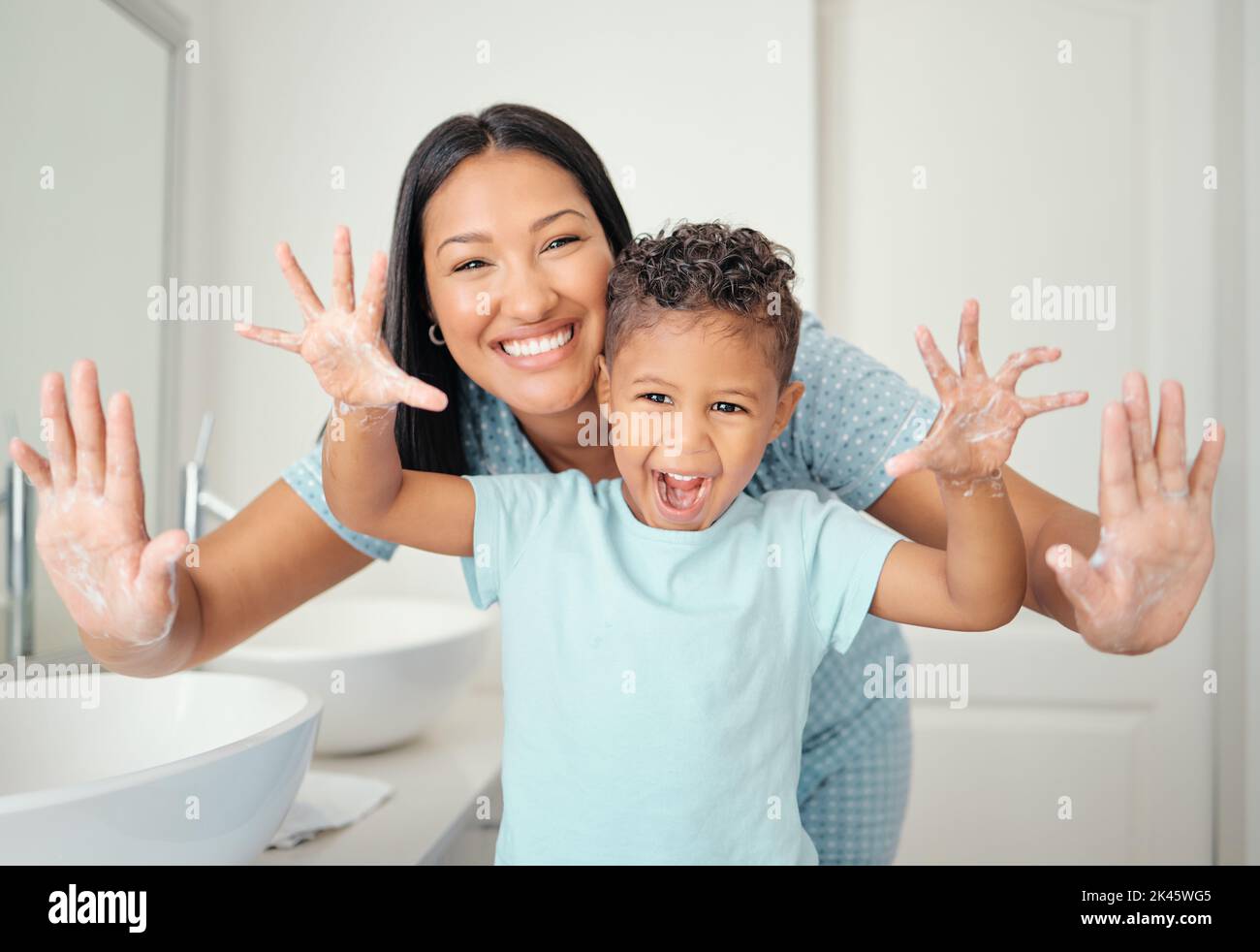 Mother and son in bathroom with clean hands, open palms that are cleaned and covered in foam teaching child hand washing. Cheerful parent help kid Stock Photo