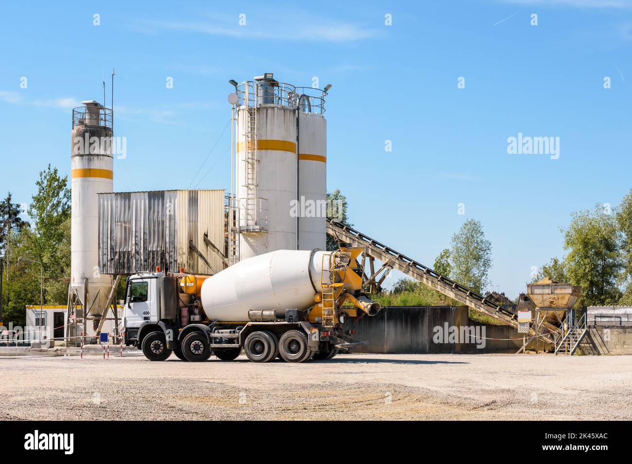 A concrete mixer truck is parked next to a sand silo in a quarry on a sunny day. Stock Photo