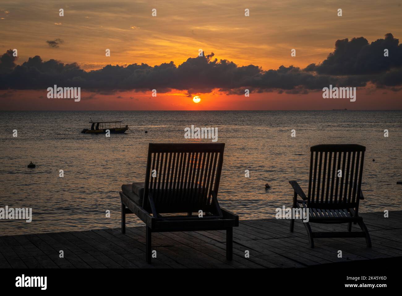 A beautiful sunrise with a peaceful, tropical setting from a shoreline sundeck highlights the beautiful morning to start a new day. Stock Photo