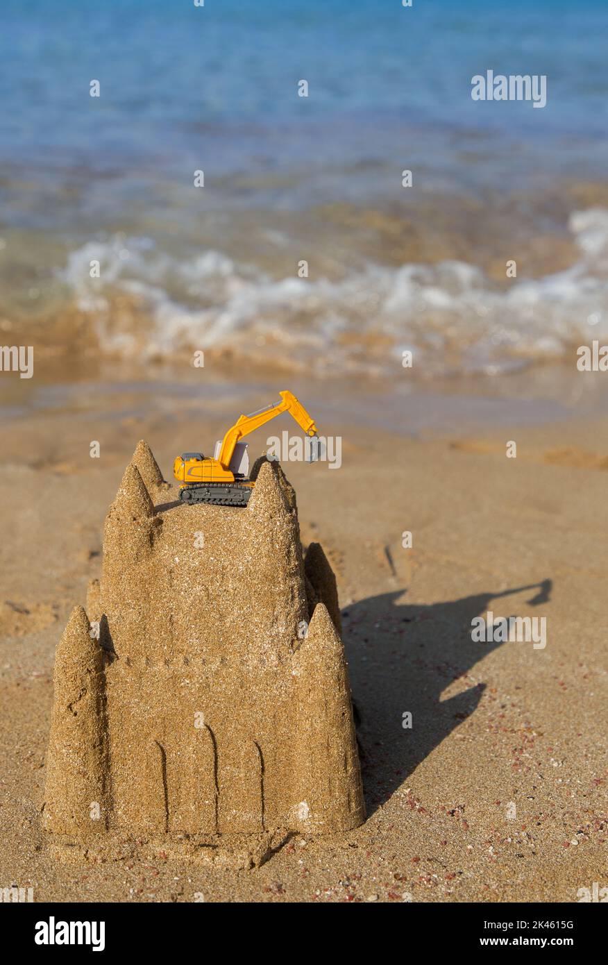 orange toy excavator stands on a castle built of coastal sand against the backdrop of the sea. Vacation in a construction company. Advertising of cons Stock Photo