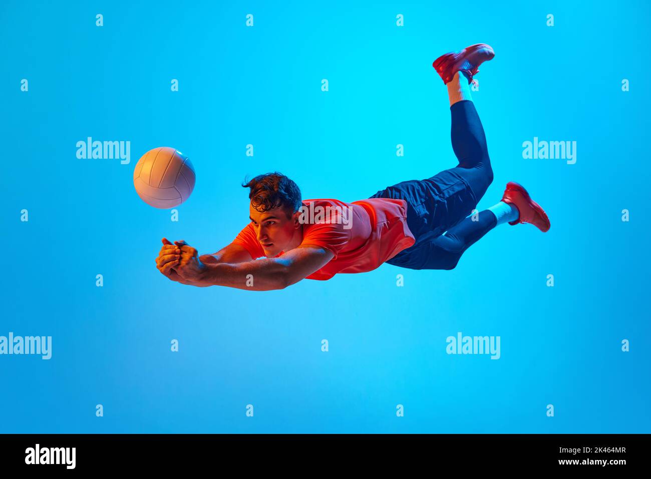 One male volleyball player in orange-black uniform training with ball isolated on blue studio background in neon light. Sport, gym, team sport Stock Photo
