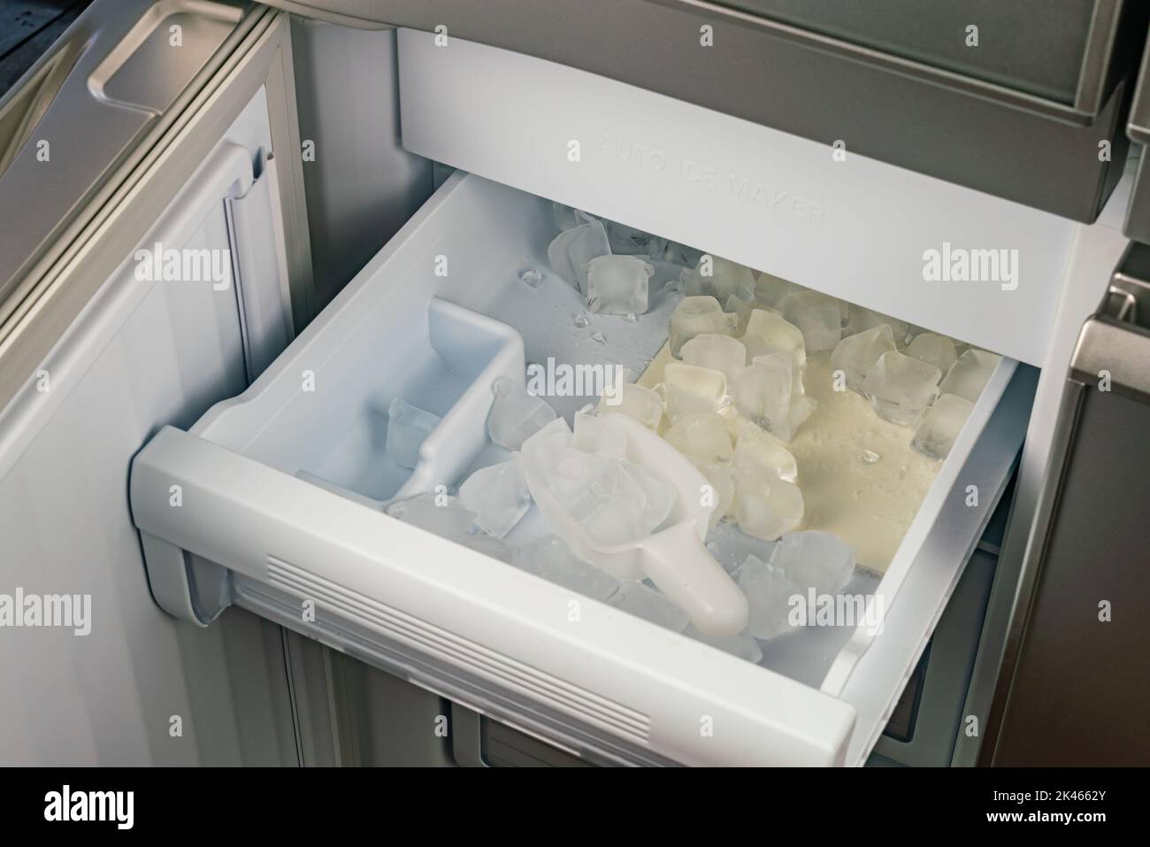 Inside of automatic ice maker with a drawer of ice cubes and plastic scoop. High angle view, closeup pile of ice cubes in a drawer of automatic ice ma Stock Photo