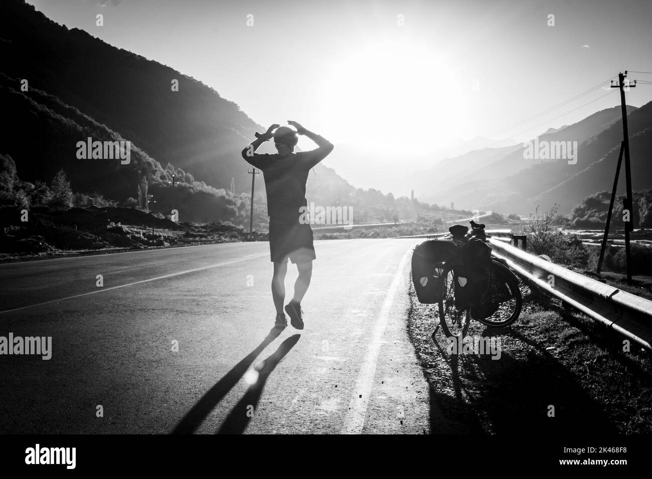 Cyclist bicycle touring frustrated with hands on his head in mountains while doing bicycle touring. Stress and fears while travel. Black and white ima Stock Photo