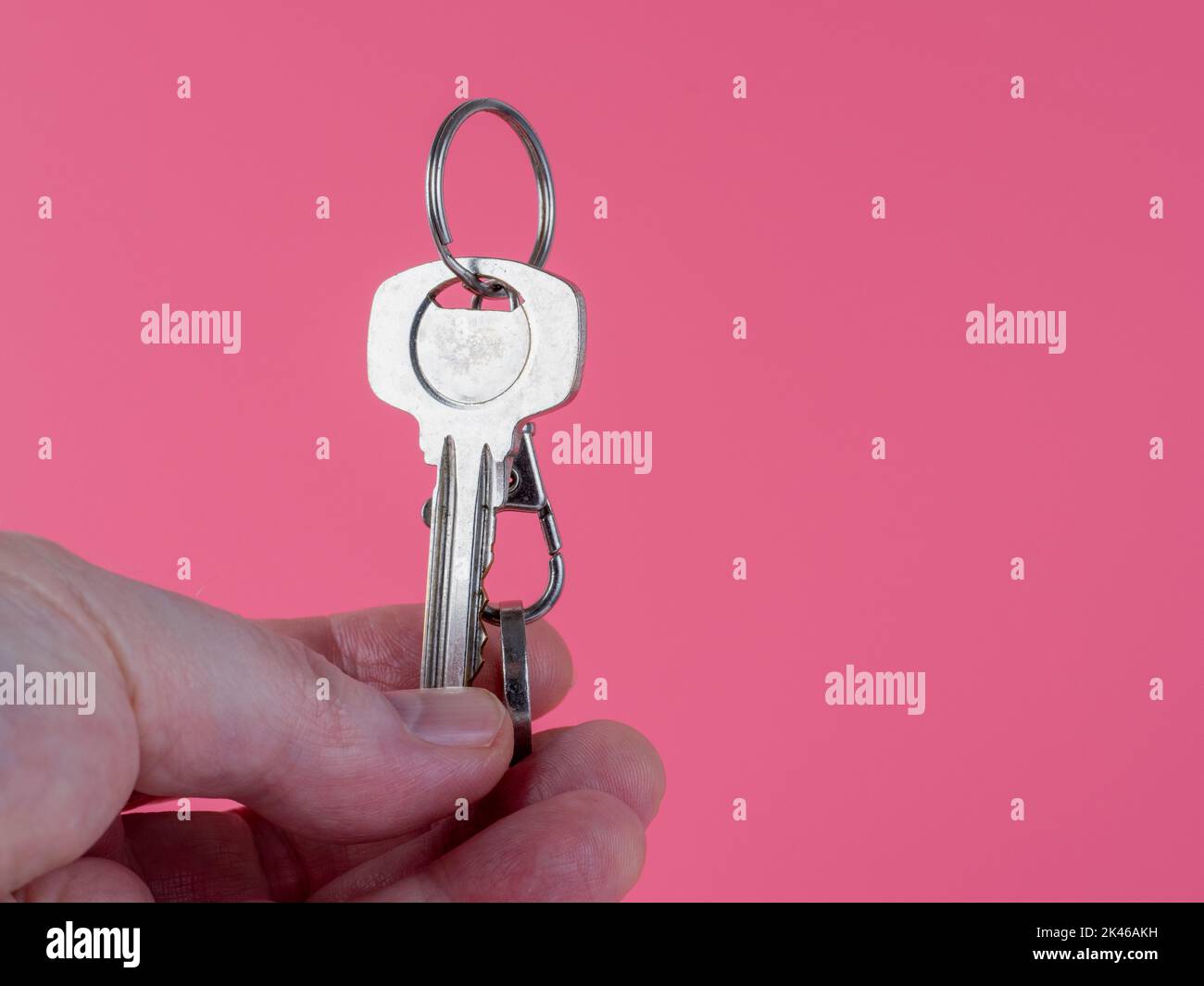 agent  holding the front door key on a key ring out to a new house  isolated against a pink background Stock Photo