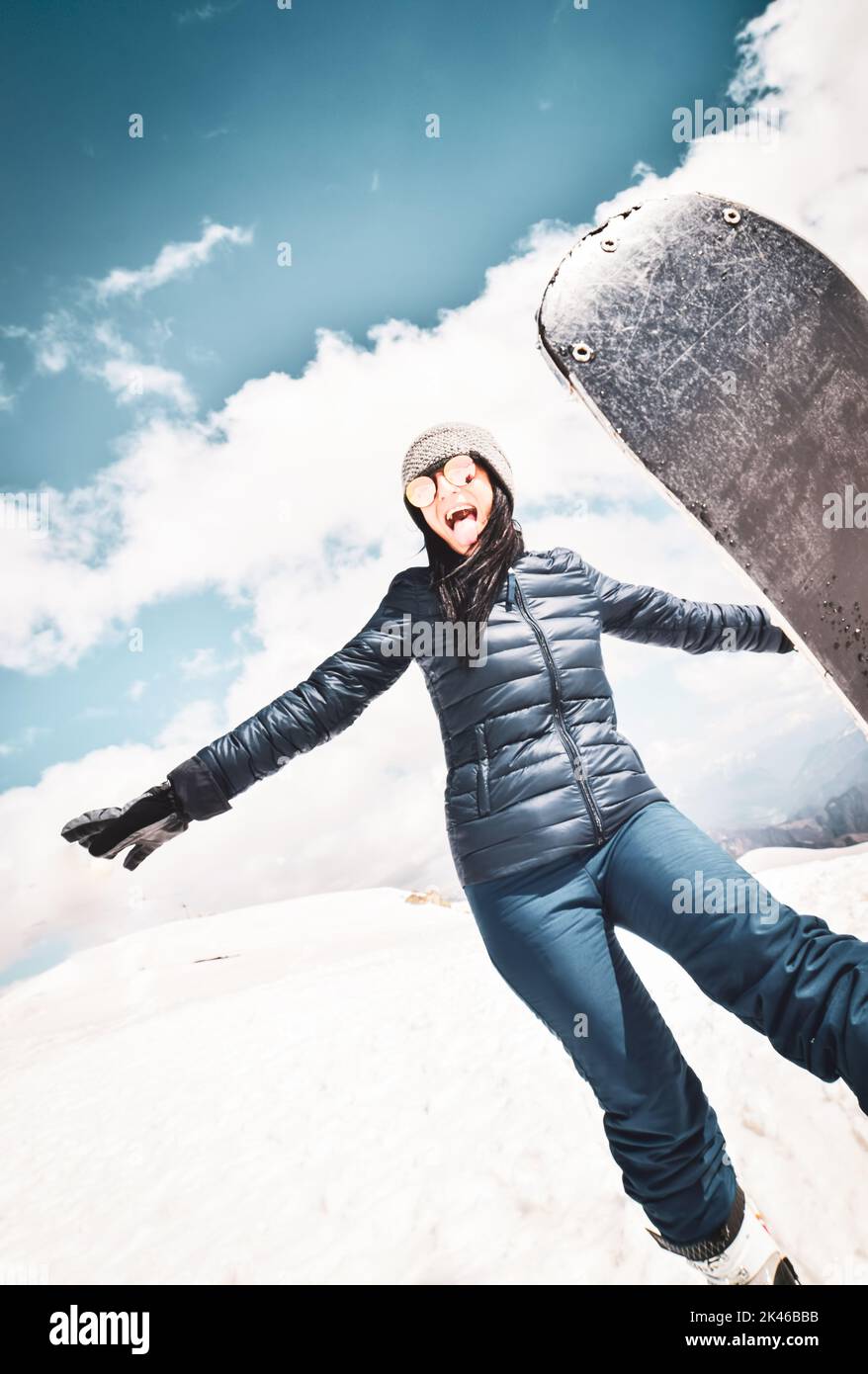 Happy excited cool caucasian brunette woman with skies pose in winter outfit in mountains. Copy paste vertical background top left Stock Photo