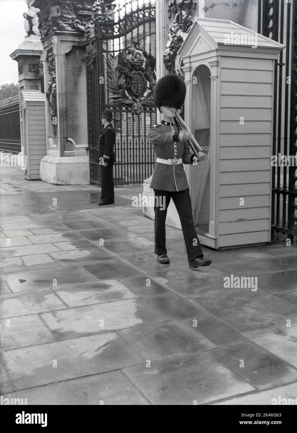 1958, historical, a policeman and a uniformed Queen's guard on duty at the entrance outside Buckingham Palace, Westminster, London, England, UK. Guardsman in their tunics and bearskins have been on sentry duty outside Buckingham Palace, the Queen's official residence, since Queen Victoria moved ther ein 1837. Stock Photo