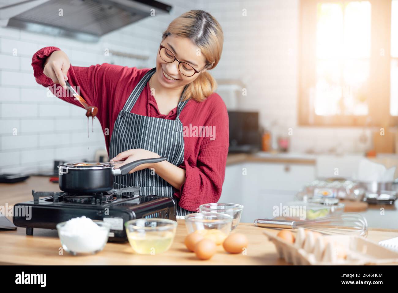 Beautiful young woman  is mixing batter, looking at camera and smiling while baking in kitchen at home ,decorating a cake of chocolate cake,cooking cl Stock Photo