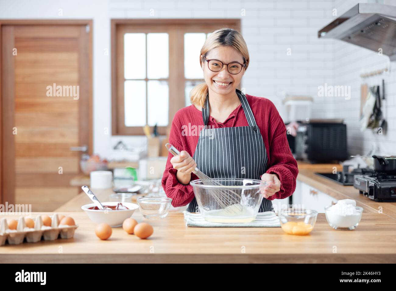 Beautiful young woman  is mixing batter, looking at camera and smiling while baking in kitchen at home ,decorating a cake of chocolate cake,cooking cl Stock Photo