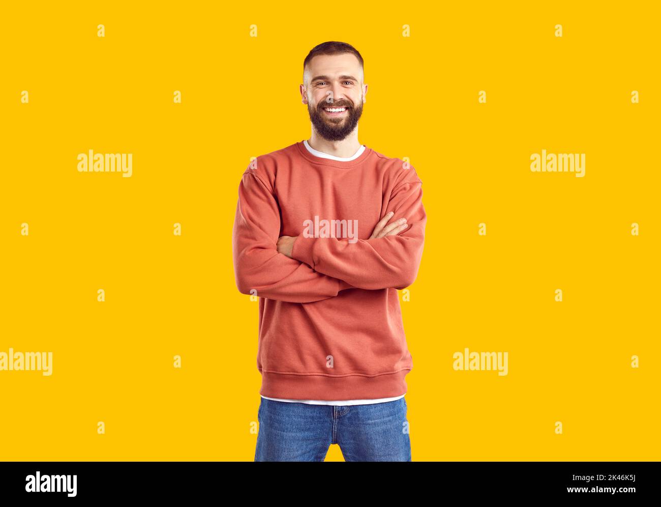 Young smiling man in red sweatshirt and jeans is posing on yellow background looking at camera. Stock Photo