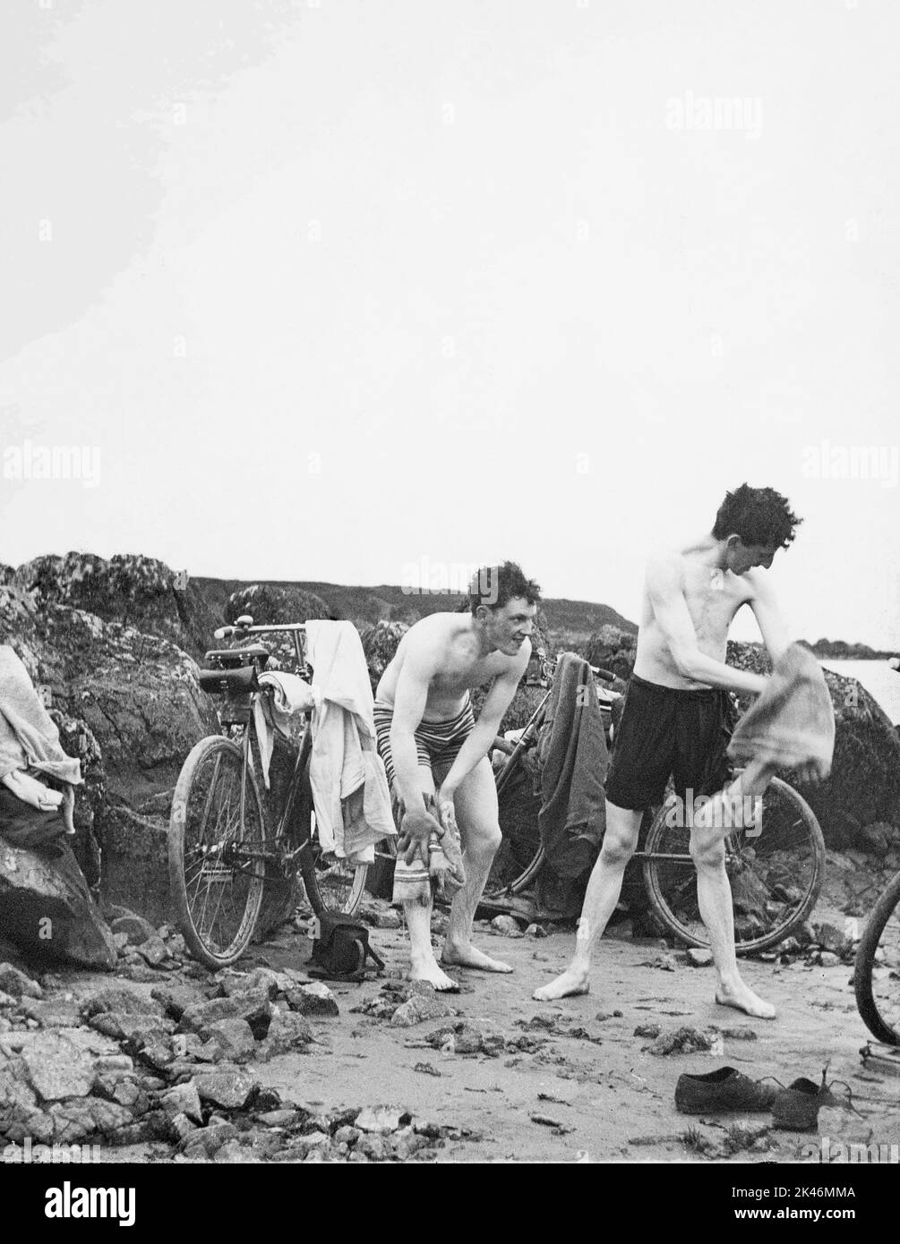 Vintage archive image from glass lantern slide dated 1901 of two young Edwardian or Victorian men towelling off a swim at the beach where they have arrived on their bicycles Stock Photo