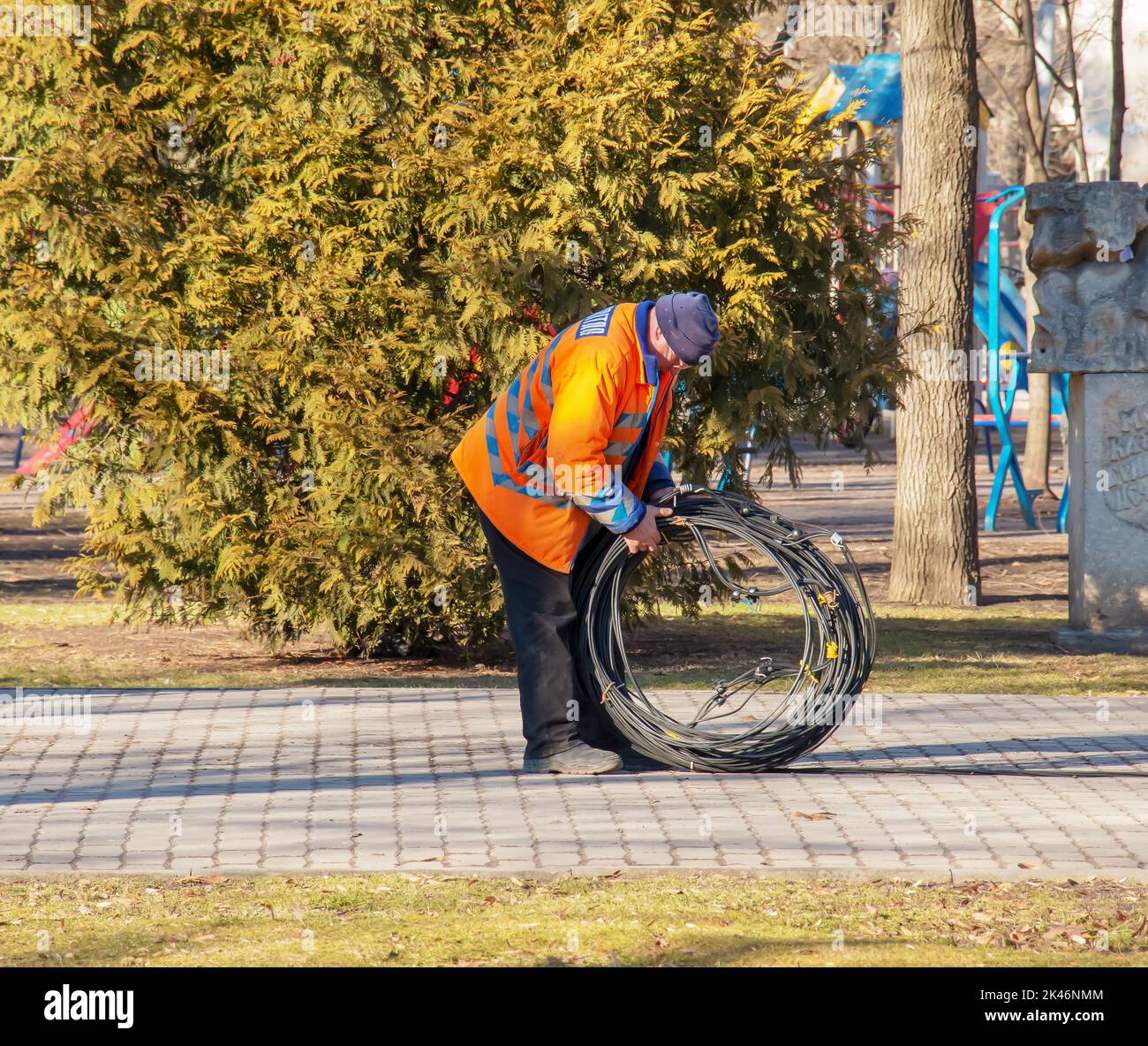 Dnipro, Ukraine - 02.15.2022: a municipal service worker in an orange uniform carries a coil of cable for further work. Stock Photo