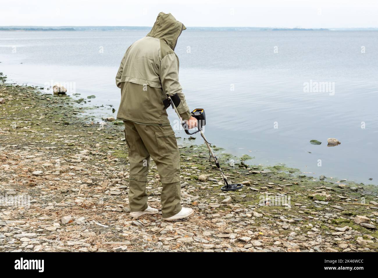 A man with a metal detector on the shore of a reservoir. Metal searches