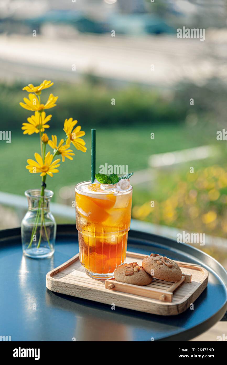 fresh homemade peach ice tea with mint, chocolate chip cookie served on table outdoors. summer cold fruit drink in sunny afternoon with yellow flowers Stock Photo