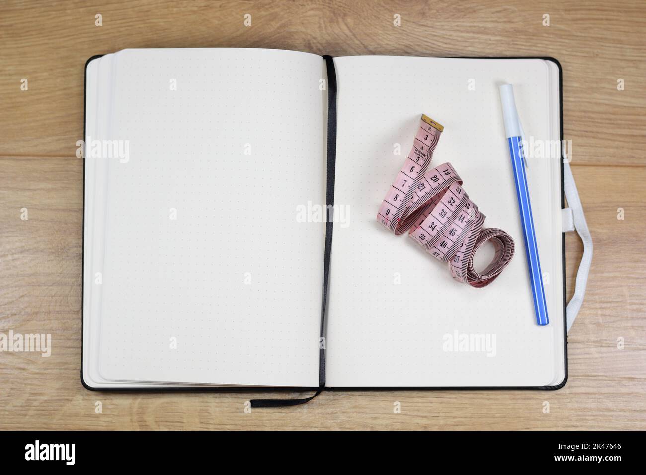Blank notebook for records, pink tailor's tape measure and blue pen on a wooden table Stock Photo