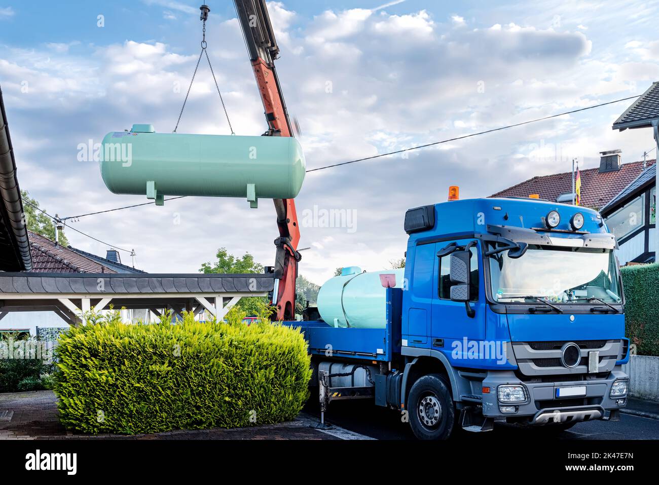 Delivery and installation of a large liquid gas tank in the garden of a residential area. Crane lifts tank into garden Stock Photo