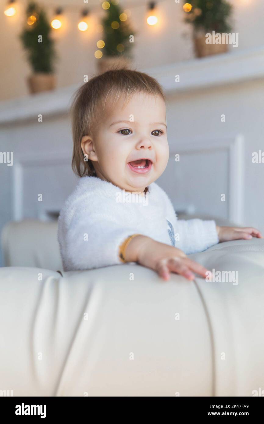 Baby on sofa is smiles so that two teeth are visible Stock Photo