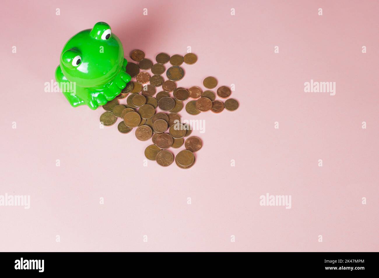 Ceramic moneybox, shape and color of green frog. Euro coins poured out from the cash bank on the pink background with copy space for text. Piggy bank. Stock Photo