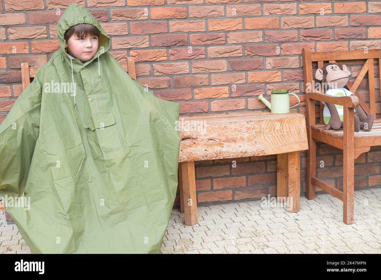 Boy in the green raincoat is sitting and waiting for raining stop. Fall