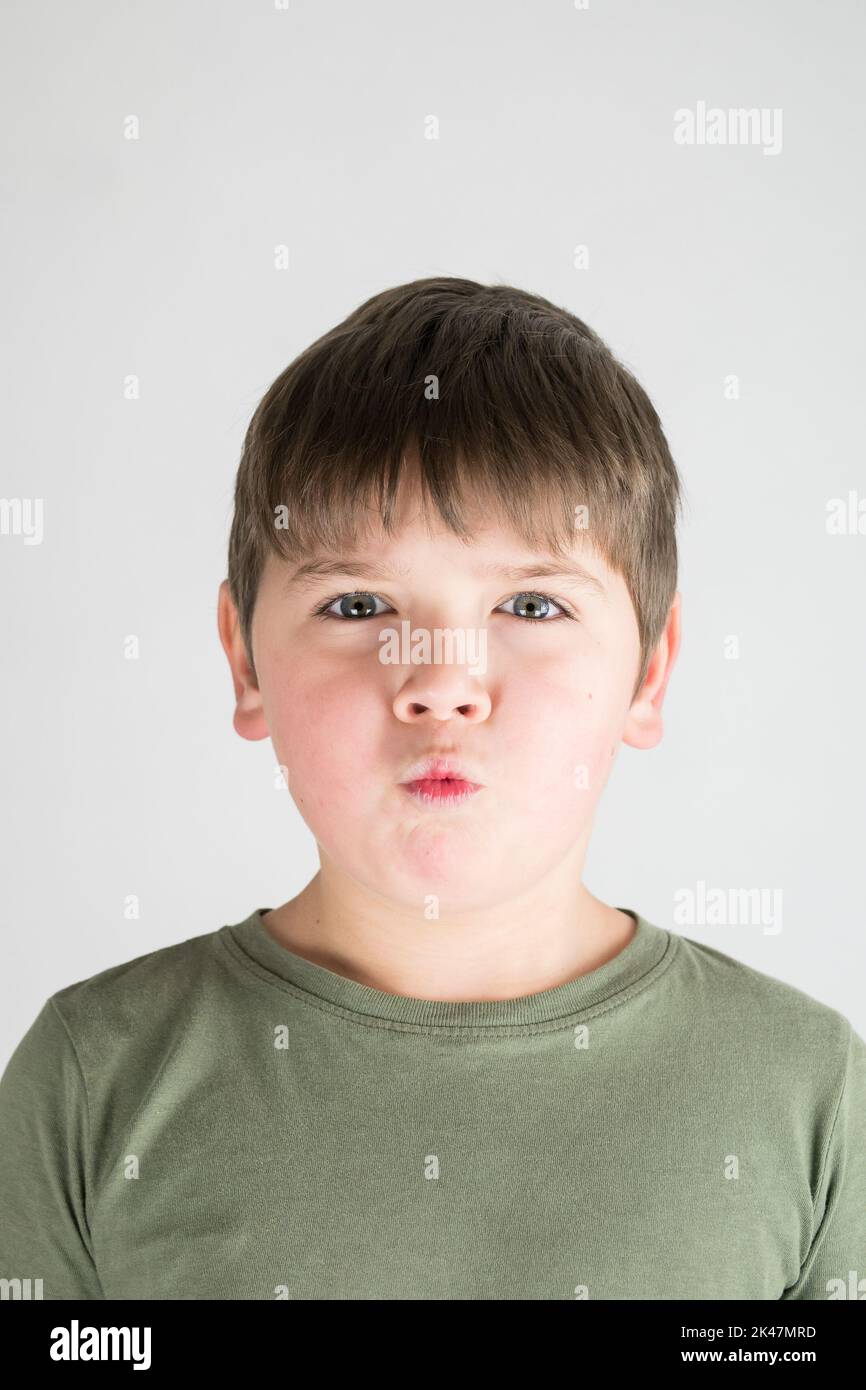 Boy, six year old portrait. Child making grimace. White background. Horizontal portrait. In green shirt. Stock Photo