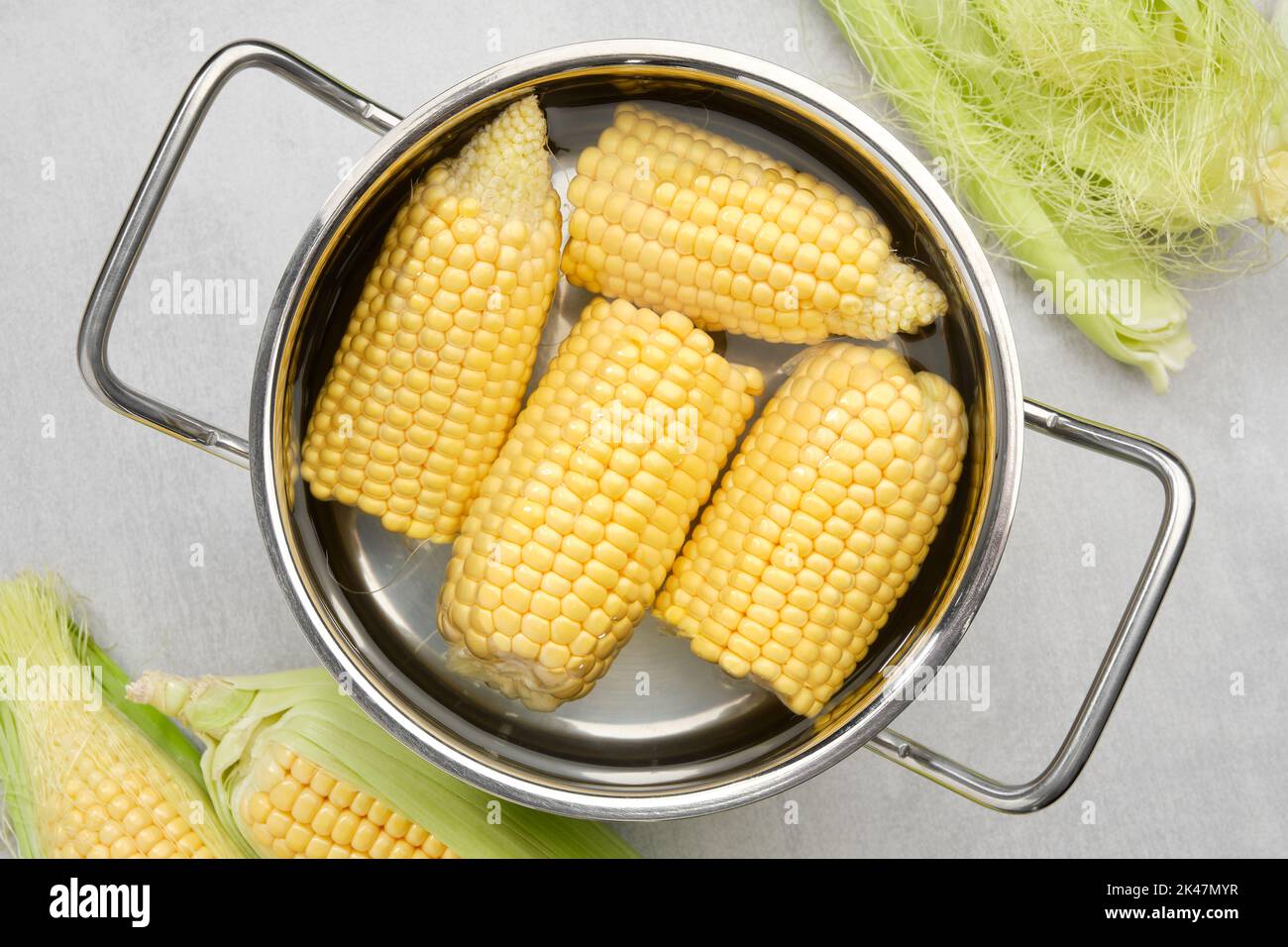 Cooking pot of yellow sweet corn cobs prepared for boiling, raw corncobs for cooking on kitchen table, top view. Stock Photo