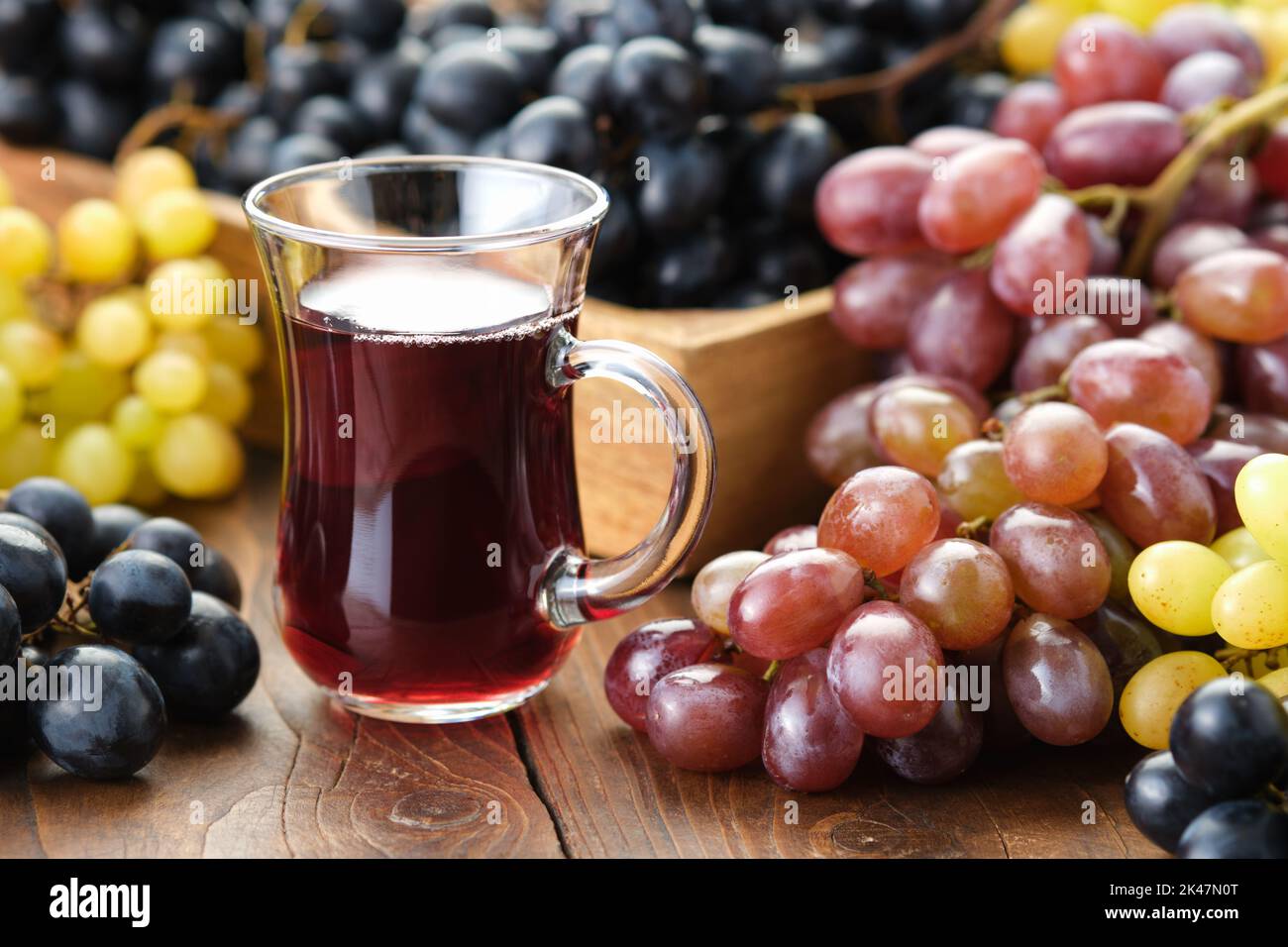 A glass cup of grape juice or wine. Black, green and purple grapes on table. Stock Photo