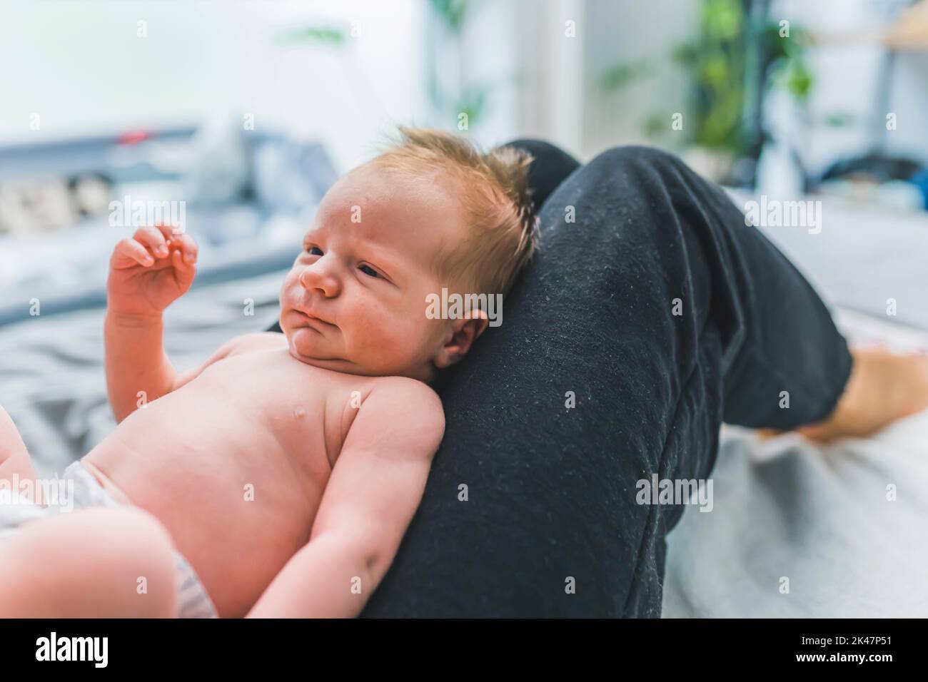 Caucasian infant boy with cute brown hair laying on his mother lap in a diaper, looking at her. High quality photo Stock Photo