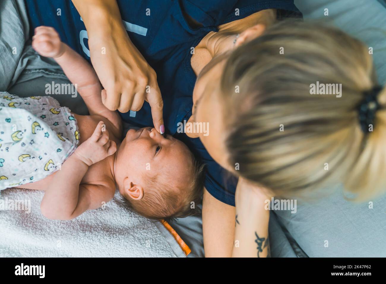 Caucasian young mom laying in bed with her couple months old baby boy, talking to him, touching his nose with her finger. Spending precious time with your child. High quality photo Stock Photo