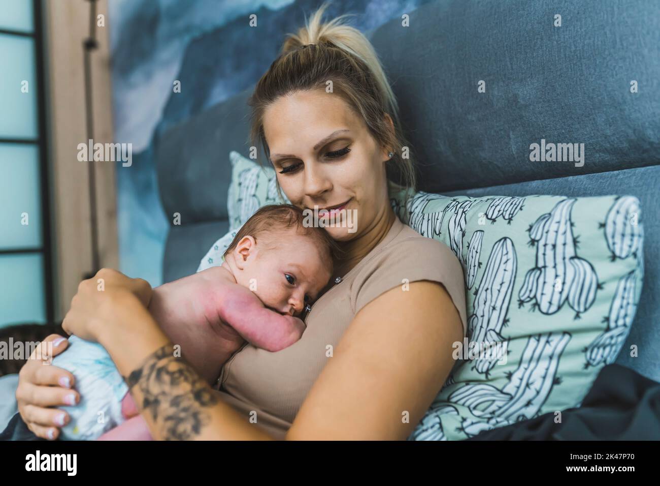 Caucasian happy young mom smiling and hugging her newborn son, who is peacefully laying in a fetal position on her chest and stomach. High quality photo Stock Photo