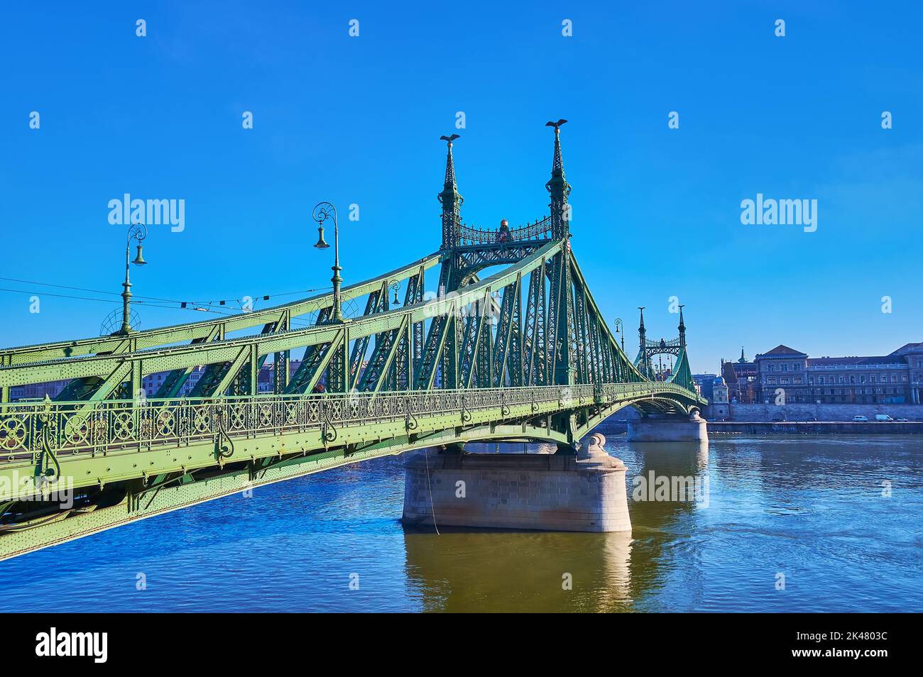 The picturesque Art Nouveau Liberty Bridge, stretching across Danube River with a view on historic building of Corvinus University on the opposite riv Stock Photo
