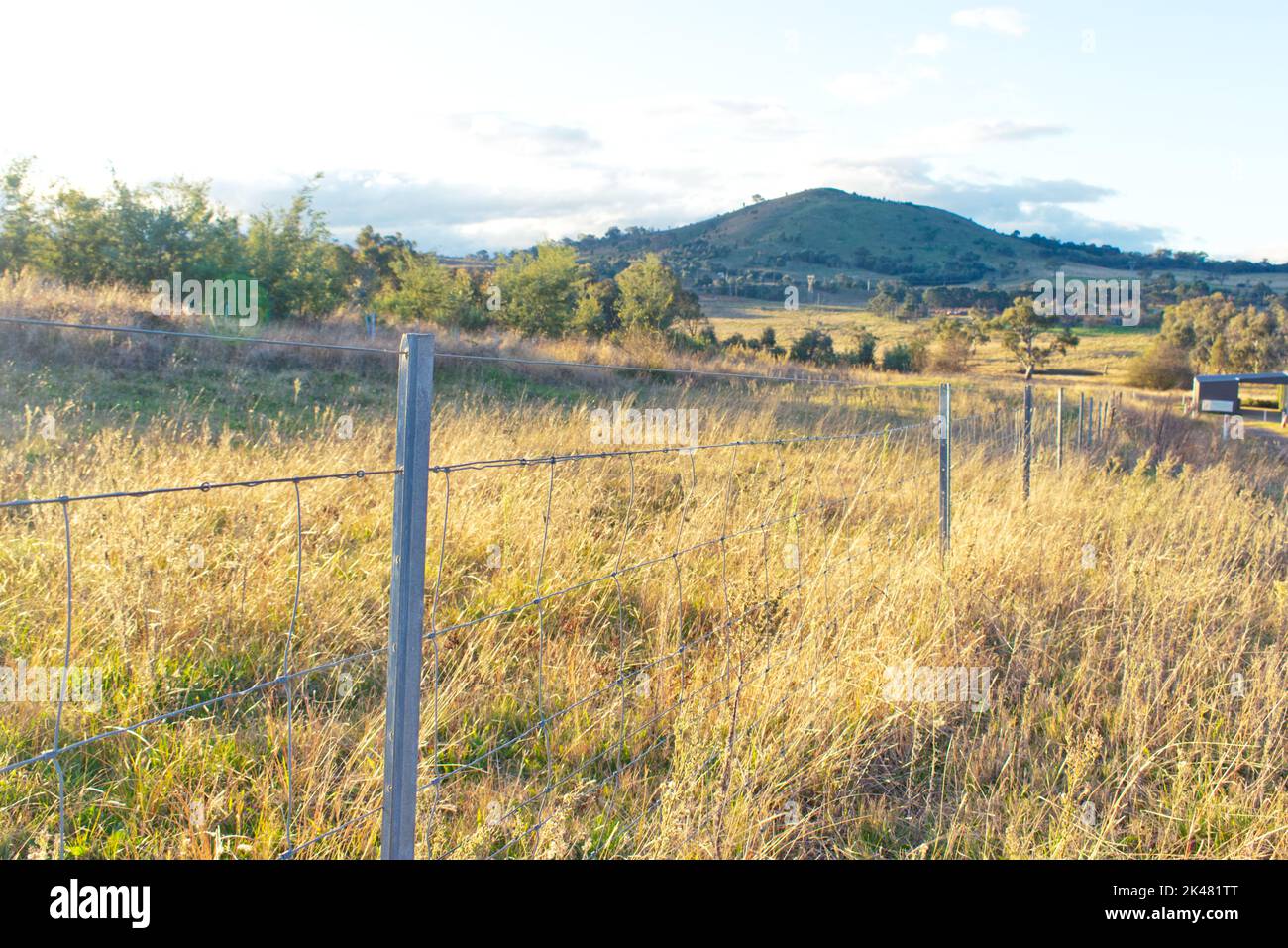 sunset as seen from a metal fence in a farming area with a mountain seen in the background Stock Photo