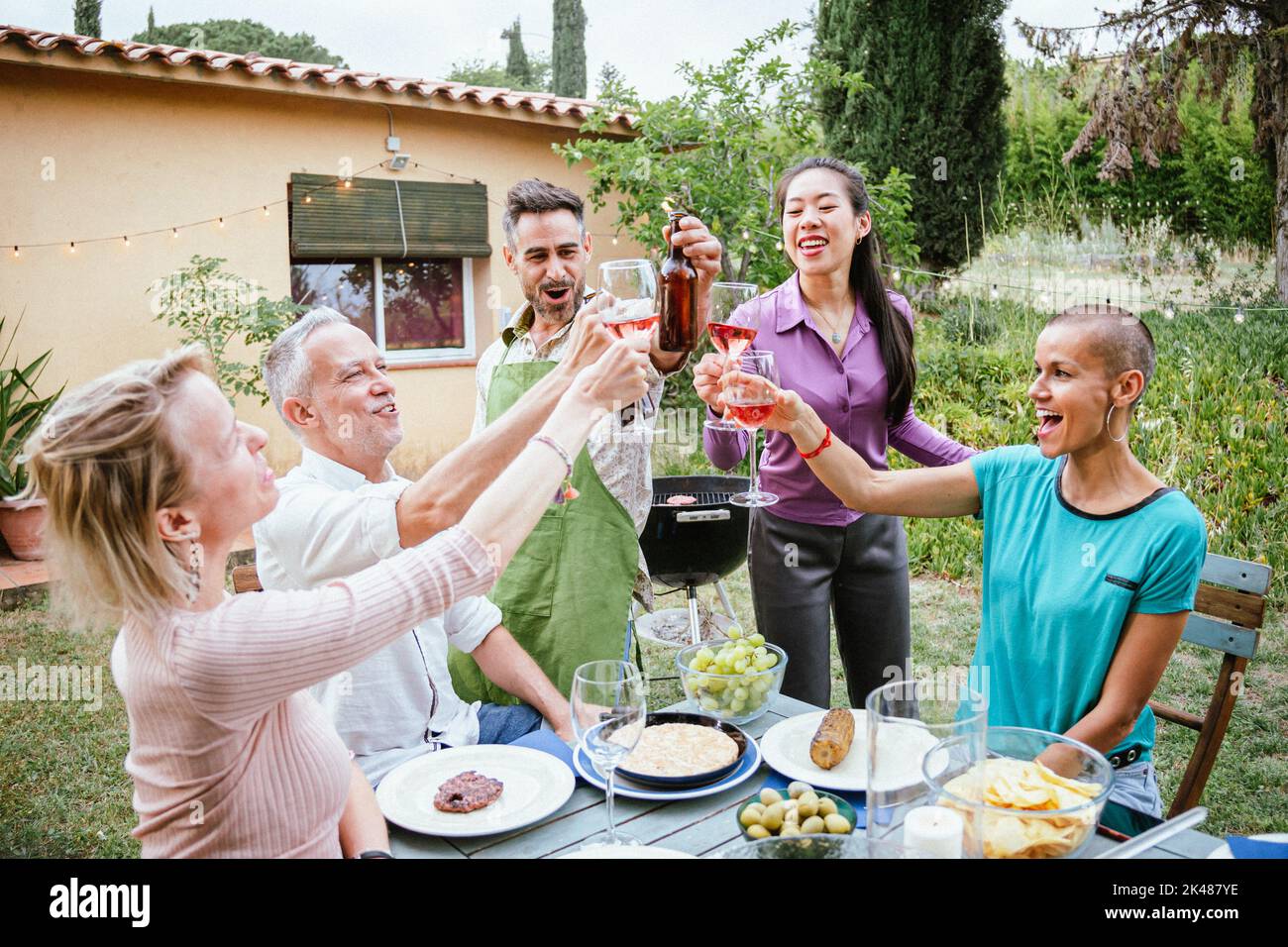 Toasting wine glasses and beers with friends at weekend event. A group of people drinking alcohol at house backyard on summer. Lifestyle concept. Stock Photo