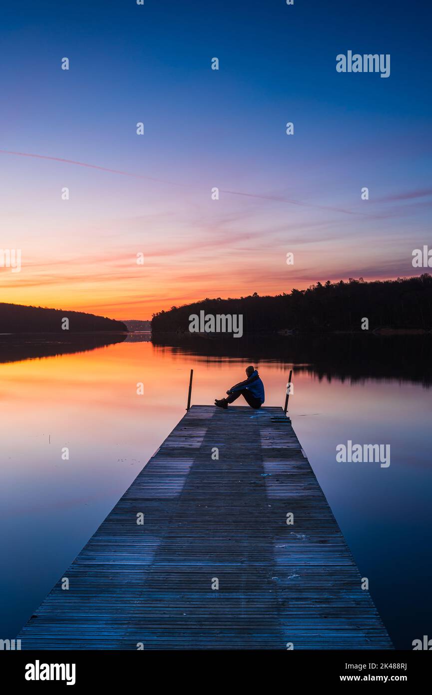 Man sitting on jetty at sunrise Stock Photo