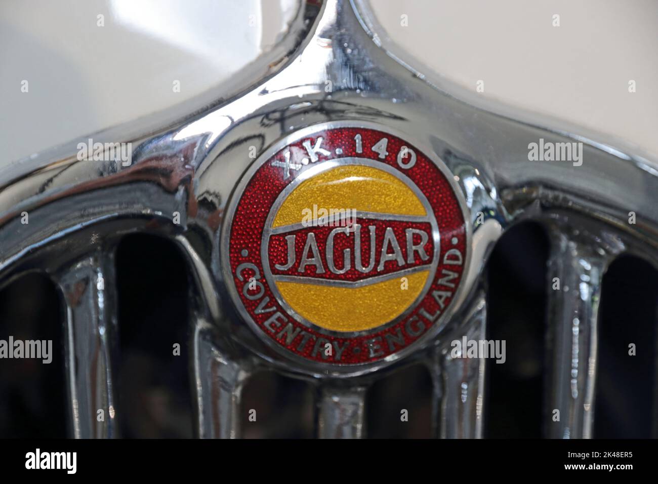 Red and gold Jaguar XK140 car badge on top of chrome radiator grille