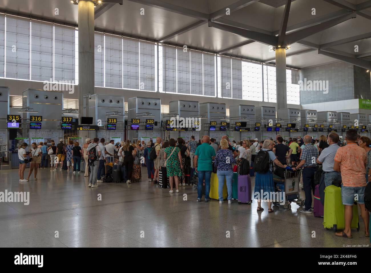 Travelers with suitcases queuing for check-in at Malaga Airport counters. Stock Photo