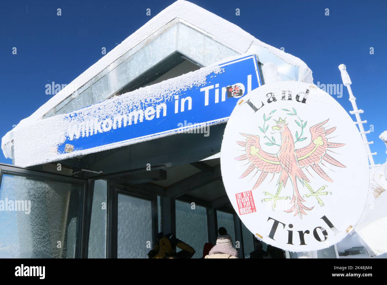 Auf der Zugspitze verläuft die Grenze zwischen Deutschland und Österreich, vor allem zwischen dem Freistaat Bayern und dem Land Tirol. Das Schild für den Freistadt ist schneebedeckt, einige Besucher betrachten das Wappen. Stock Photo