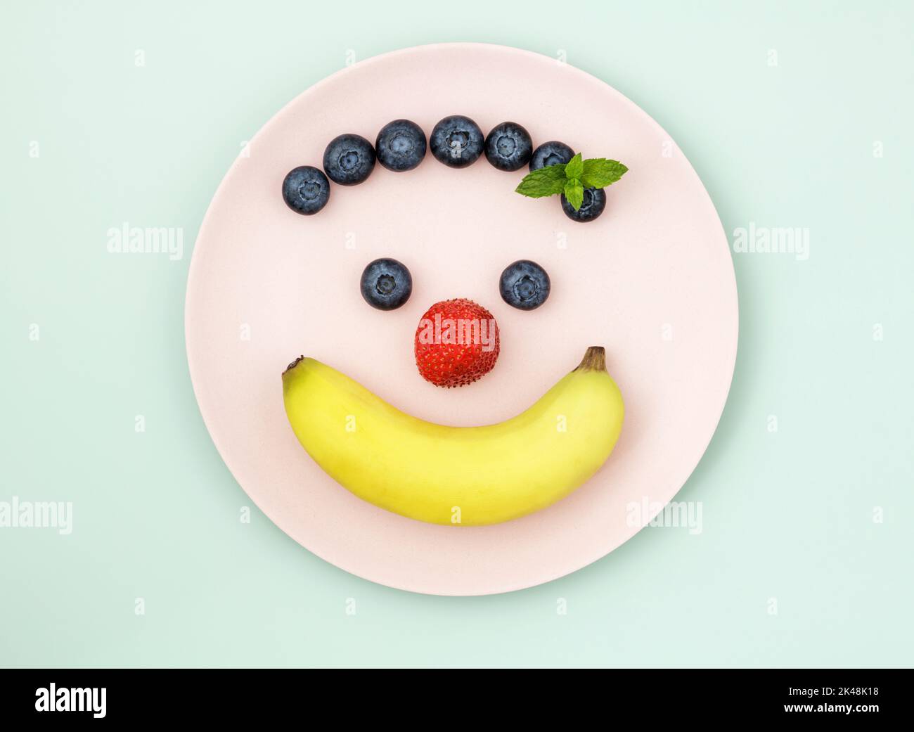 Banana and berries on pink plate arranged in the shape of a happy face Stock Photo
