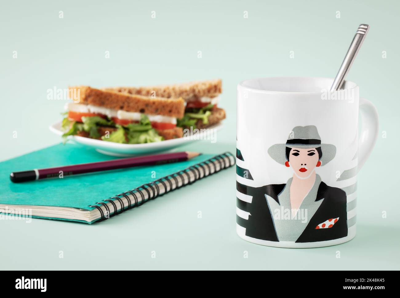 White mug with art deco style painting, sandwich and green notebook Stock Photo