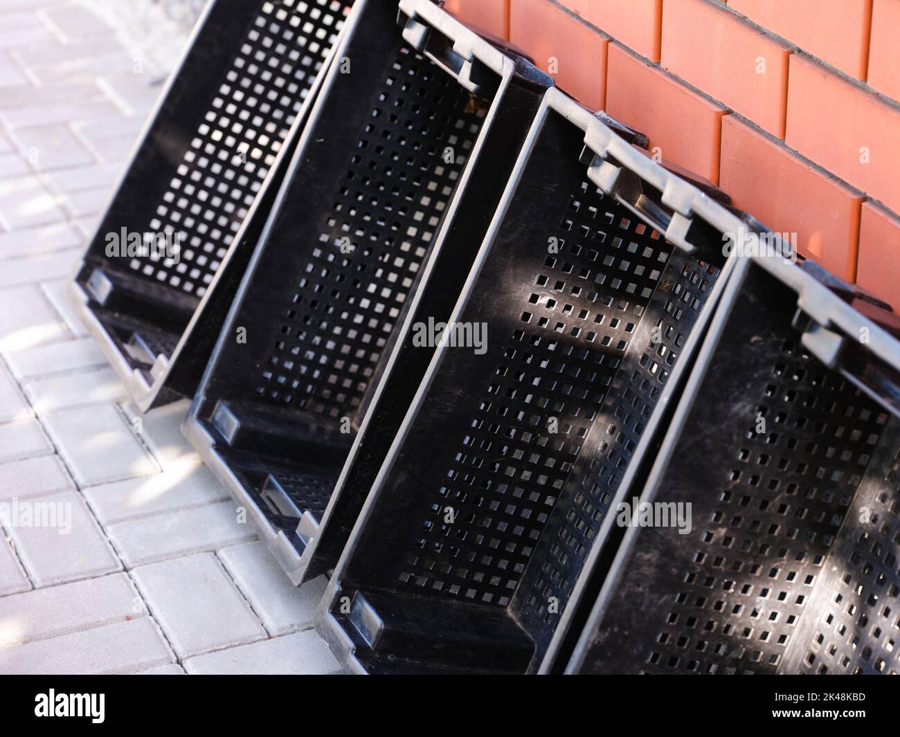 Four empty black plastic crates for fruits and vegetables standing leaning against a brick wall outdoors Stock Photo