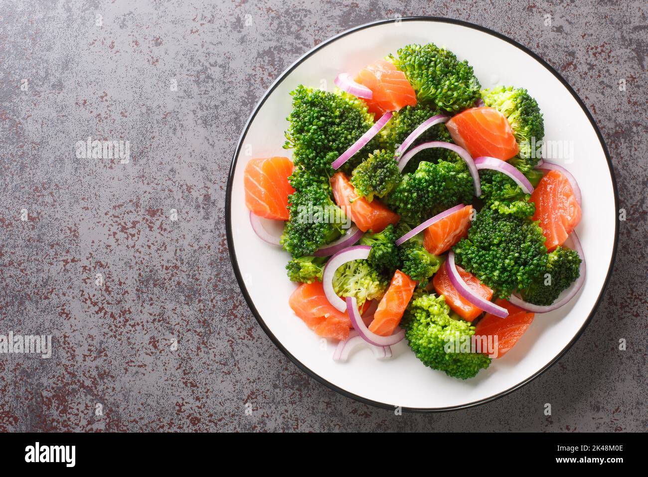 Natural mix salad of boiled broccoli, salted salmon and fresh red onion close-up in a plate on the table. horizontal top view from above Stock Photo