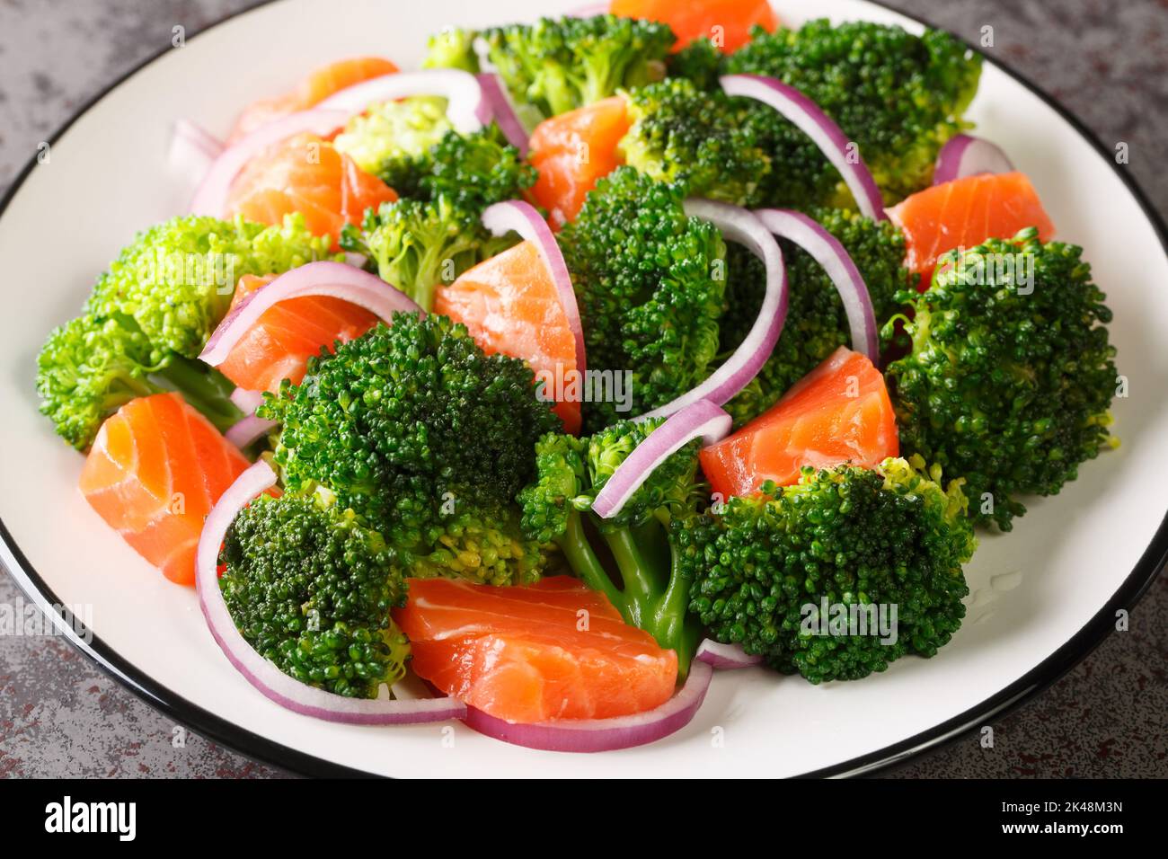 Fresh healthy salad of boiled broccoli, smoked salmon and red onion close-up in a plate on the table. horizontal Stock Photo